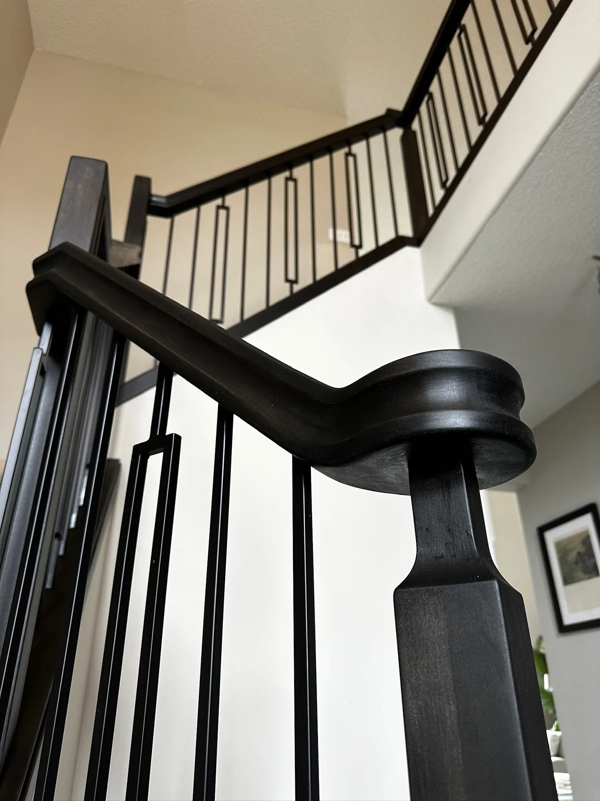 Dark stained wood handrail with a volute scroll and metal spindles on a custom Edmonton staircase